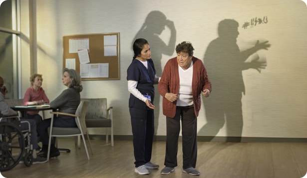 Female patient shows signs of Agitation associated with dementia due to Alzheimer's disease in a care home while being tended by a nurse, with shadow imagery showing the nurse’s anguish as the patient uses foul language.